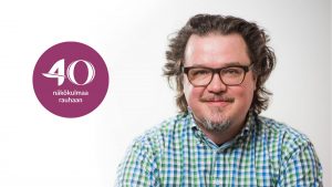 Tomi Kiilakoski hymyilee kameralle sini-vihreässä kauluspaidassa.