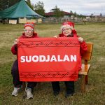 Annikki Peltovuoma ja Eila Magga istuvat "Suojelen" -kyltin kanssa.