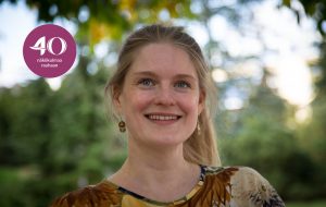 Jenni Leppänen katsoo yläviistoon vihreä lehvästö taustallaan.