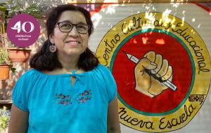 Marlene Soto Godoy seisoo seinän edessä, johon on maalattu keltainen nyrkki, joka pitelee kynää.