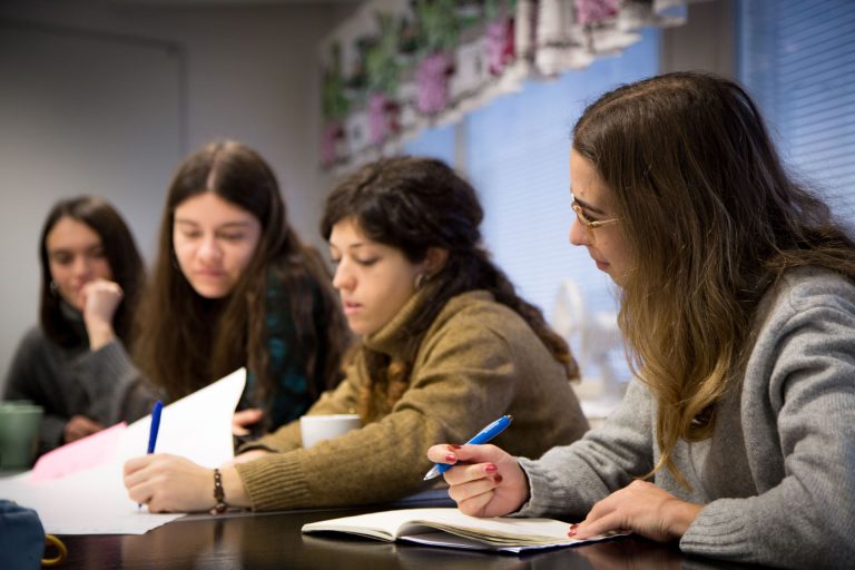 An image of four people sitting at a table. One of them is taking notes and the others are looking at the notes.