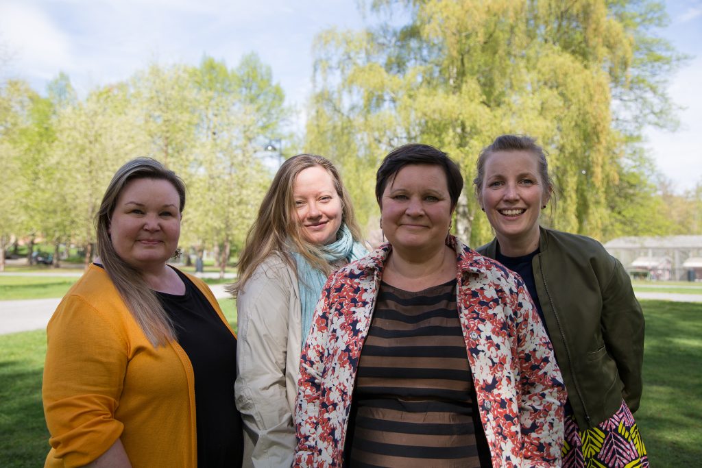 RKI:n työntekijät Riikka Jalonen, Mari-Anne Okkolin, Elina Lauttamäki ja Heli Pekkonen hymyilevät kameralle puistossa.